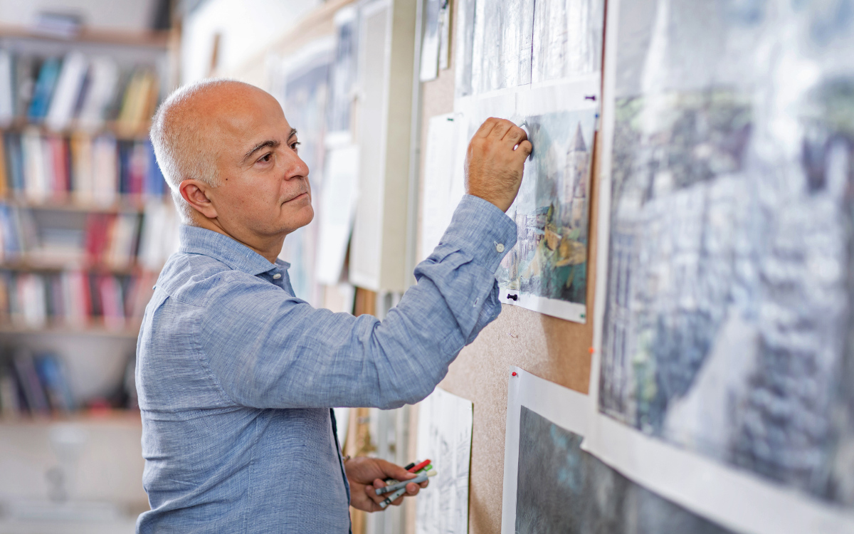 Der Panoramakünstler Yadegar Asisi zeichnet an einer Pinnwand mit Entwürfen und Bildskizzen im Atelier.