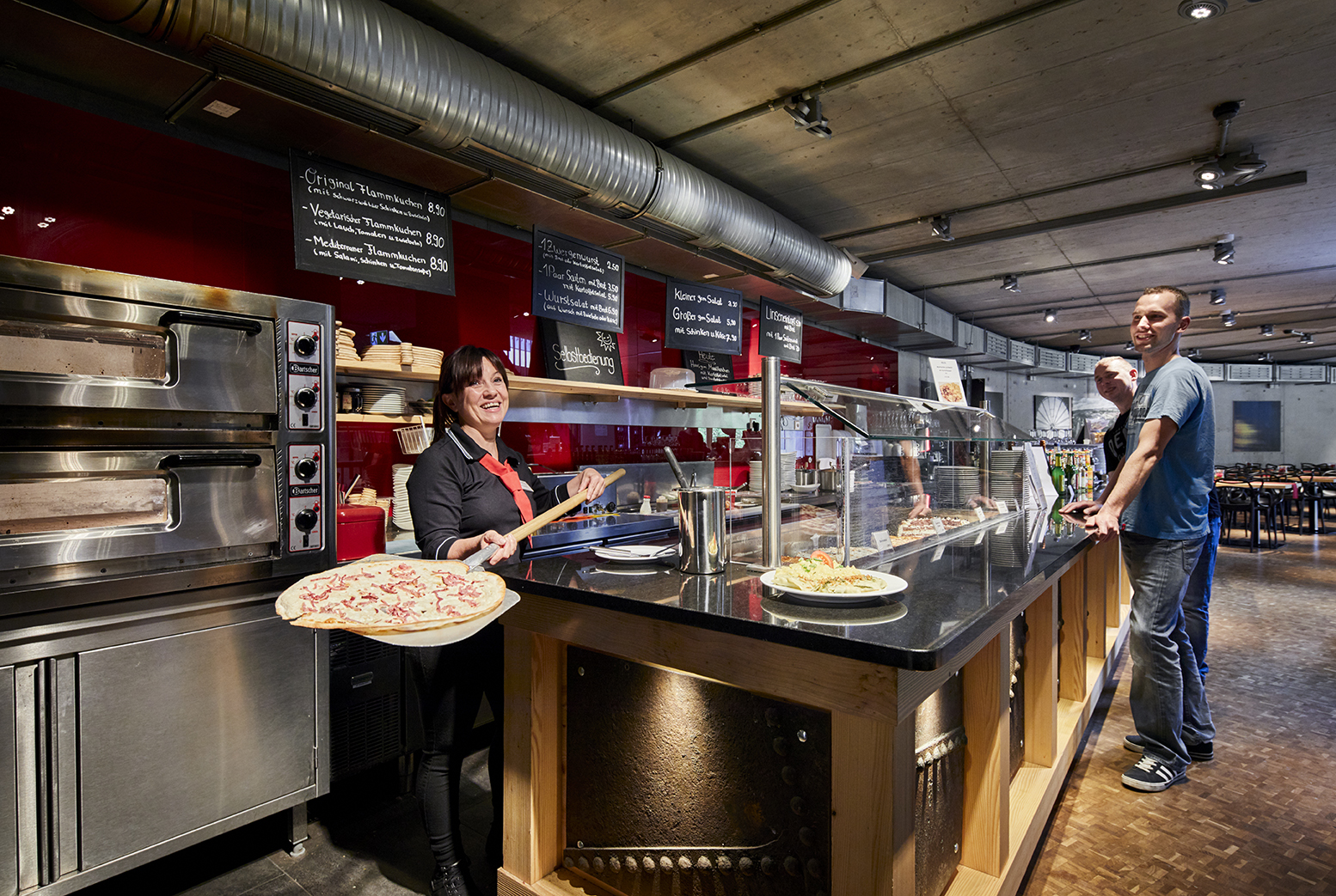 Bistrotheke mit Flammkuchen, hinter der eine Mitarbeiterin Gäste bedient.