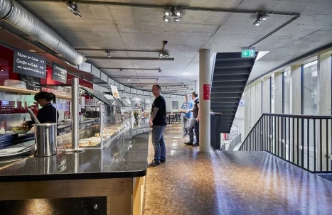 Bistrobereich im Obergeschoss mit Theke, Treppe und mehreren Besuchern in moderner Innenarchitektur.